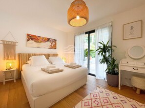 A bedroom with a bed, bedside lamps, a large window, a potted plant, a dresser, and a painting on the wall. - Villa ALOITA (SEIGNOSSE)