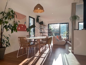 A spacious dining area with a wooden table and chairs, surrounded by large windows and plants.