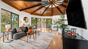 A spacious living area with a modern ceiling design, a large flat-screen TV, and a dining area with a table and chairs. - Via Vallarta - An Architecturally Significant California Modern Home (Encino)