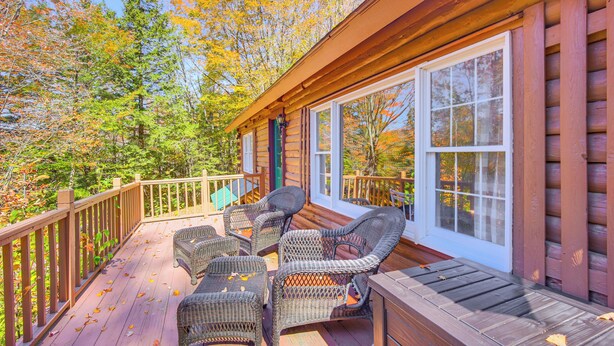 A wooden deck with wicker furniture, a glass door, and a view of autumn trees. - Andover Cabin Retreat w/ Hot Tub & Fireplace! (Andover)