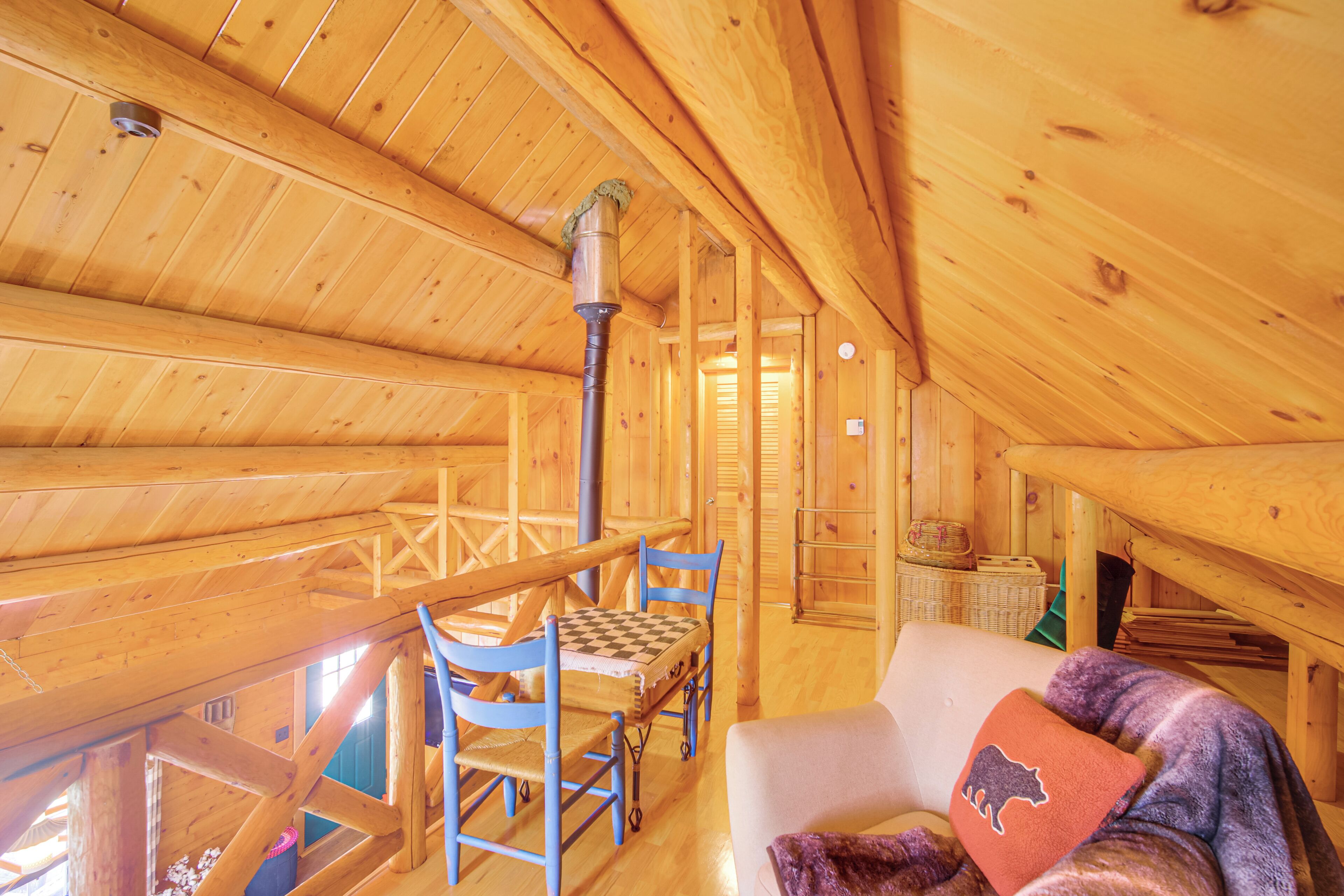 A wooden cabin interior with a high ceiling, a checkered table, blue chairs, a white sofa, and a buffalo-themed pillow.