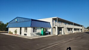 Un motel avec un auvent bleu et un magasin 7-Eleven vert. Il dispose d’un parking couvert et d’un bâtiment à deux étages doté d’un balcon.