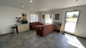 Un espace d’accueil comprenant un canapé, une petite table, une poubelle, un four à micro-ondes et un présentoir à livres.