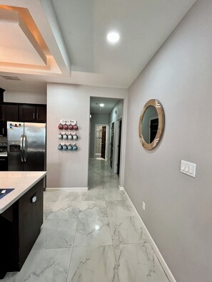 A modern kitchen with a stainless steel refrigerator, a marble-tiled floor, and a hallway leading to a bedroom.
