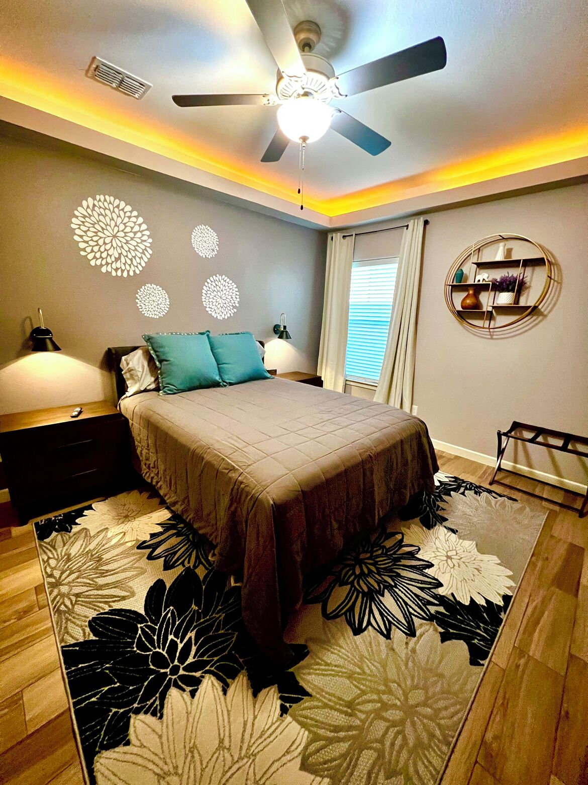 A bedroom with a bed, nightstands, a ceiling fan, decorative wall art, and a window with curtains.