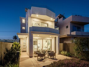 A modern two-story house with a patio, outdoor furniture, and a visible address number.