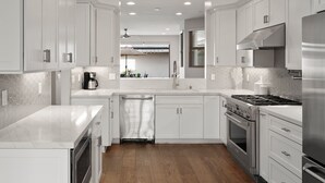 A modern kitchen with white cabinetry, stainless steel appliances, and a wooden floor. - Large Family Beach Home | 1 Block to Beach & More | AC (San Diego)