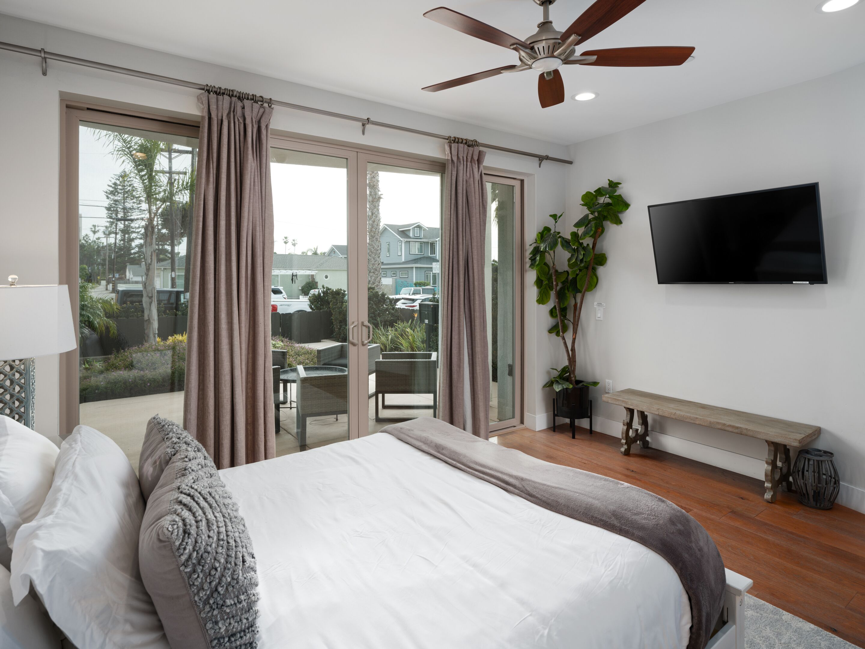 Una camera da letto con un letto grande, un ventilatore a soffitto, una TV e un balcone con tende.