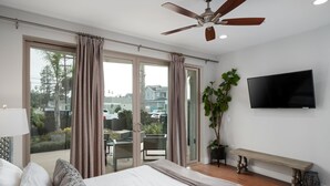 A bedroom with a large bed, a ceiling fan, a TV, and a balcony with curtains. - Large Family Beach Home | 1 Block to Beach & More | AC (San Diego)