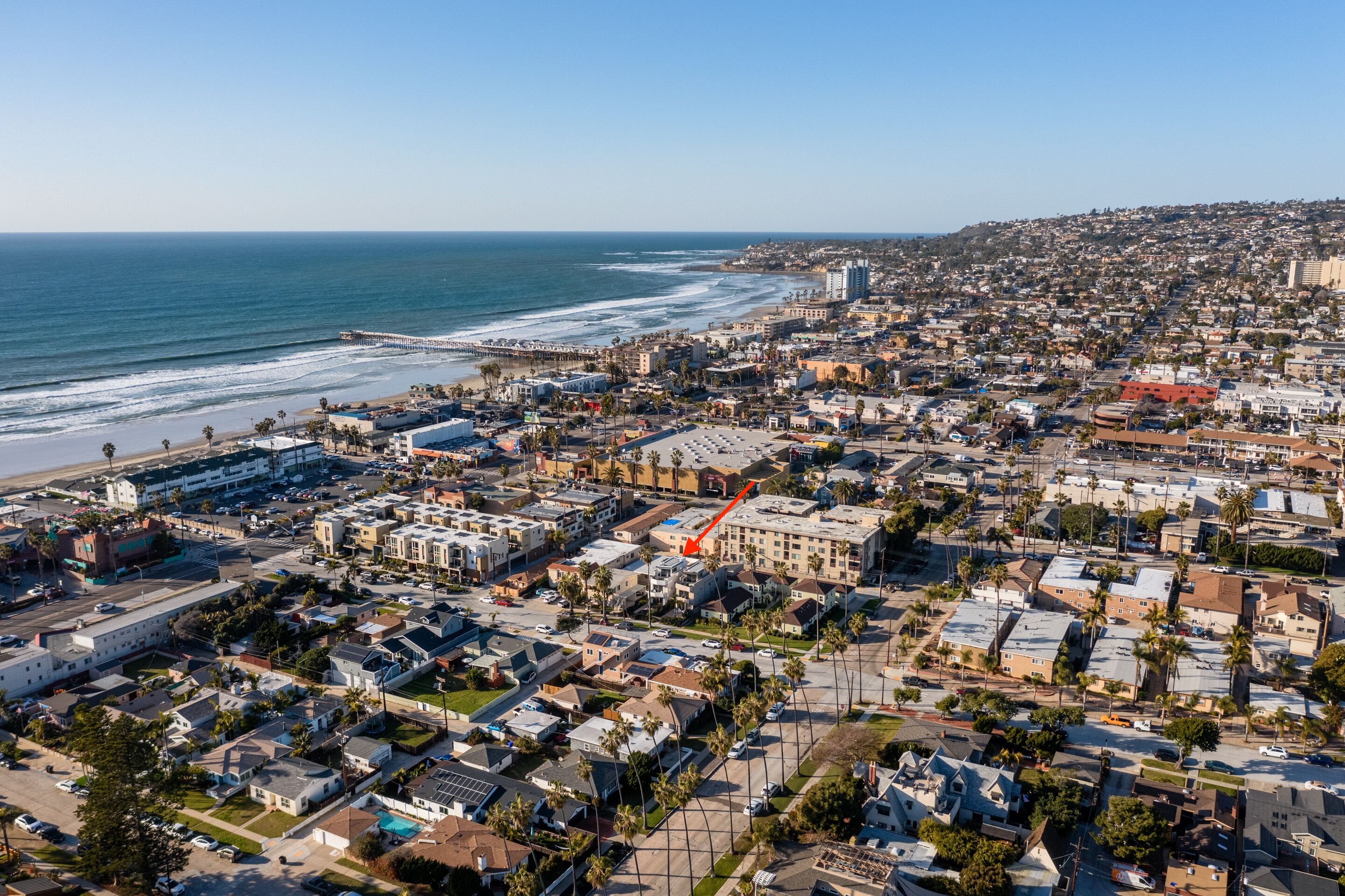 An aerial view of a coastal city with a beach, residential areas, and a prominent red building marked by an arrow.