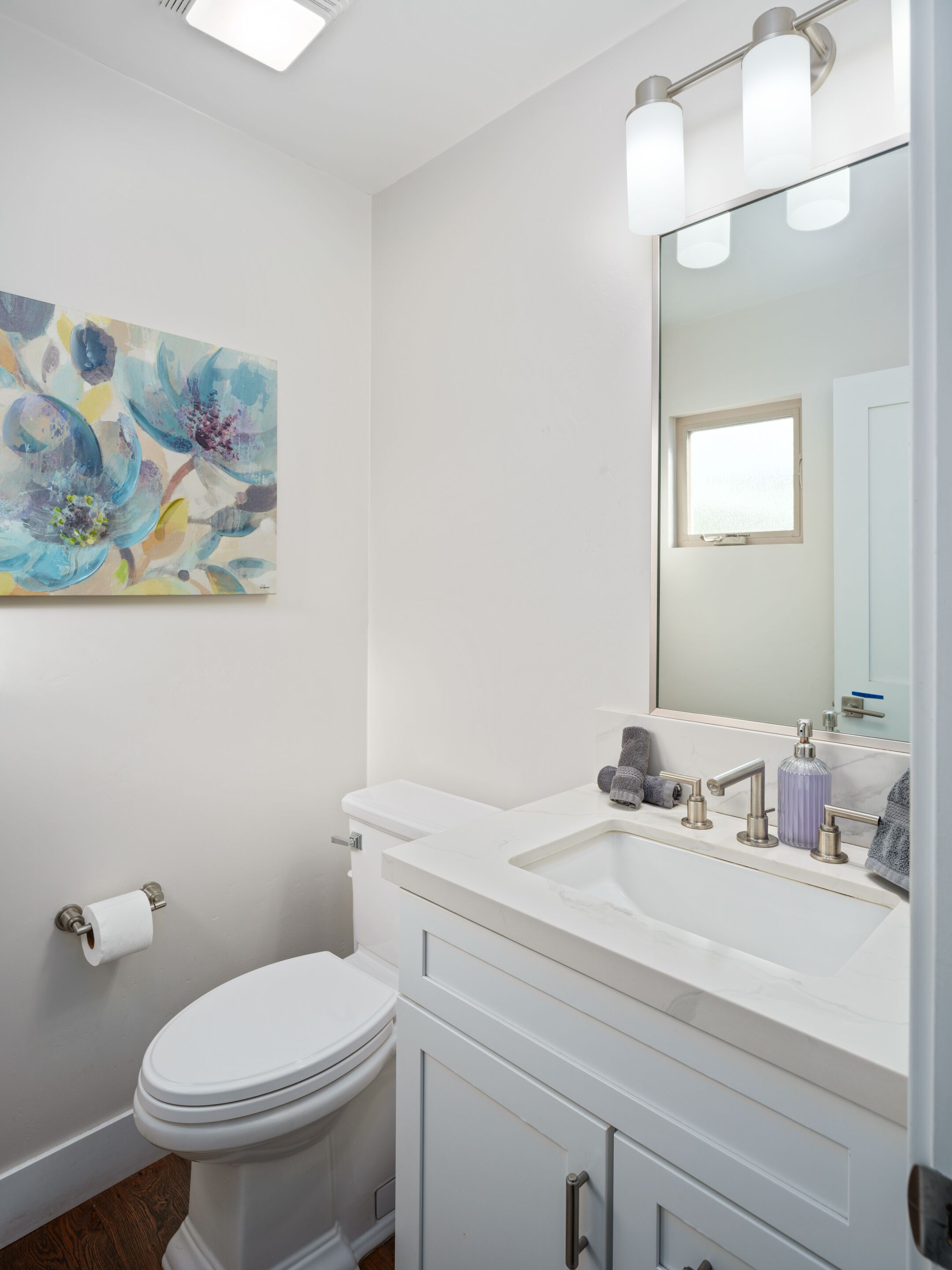 A modern bathroom with a white toilet, a sink with a mirror, and a painting on the wall.
