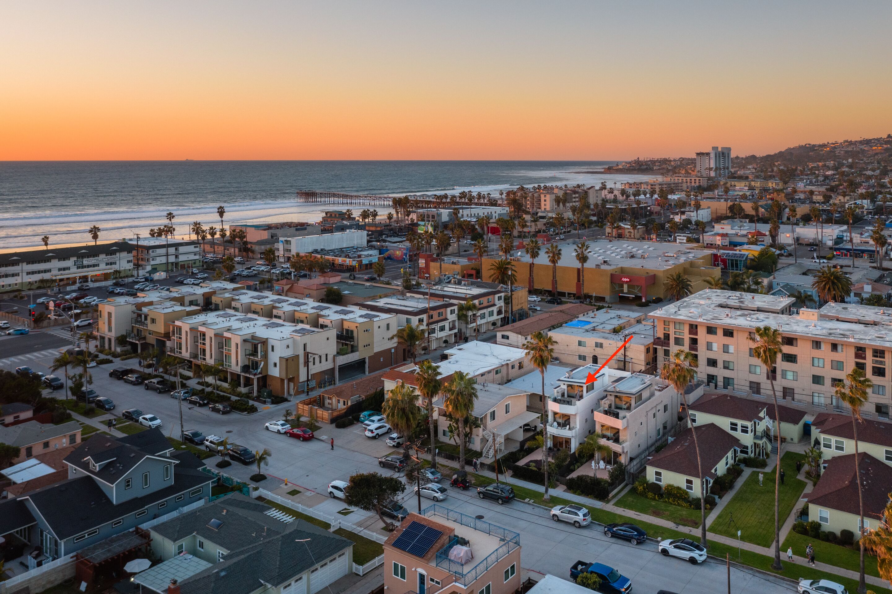 A coastal residential area with multi-story buildings, a visible beach, and a pier.