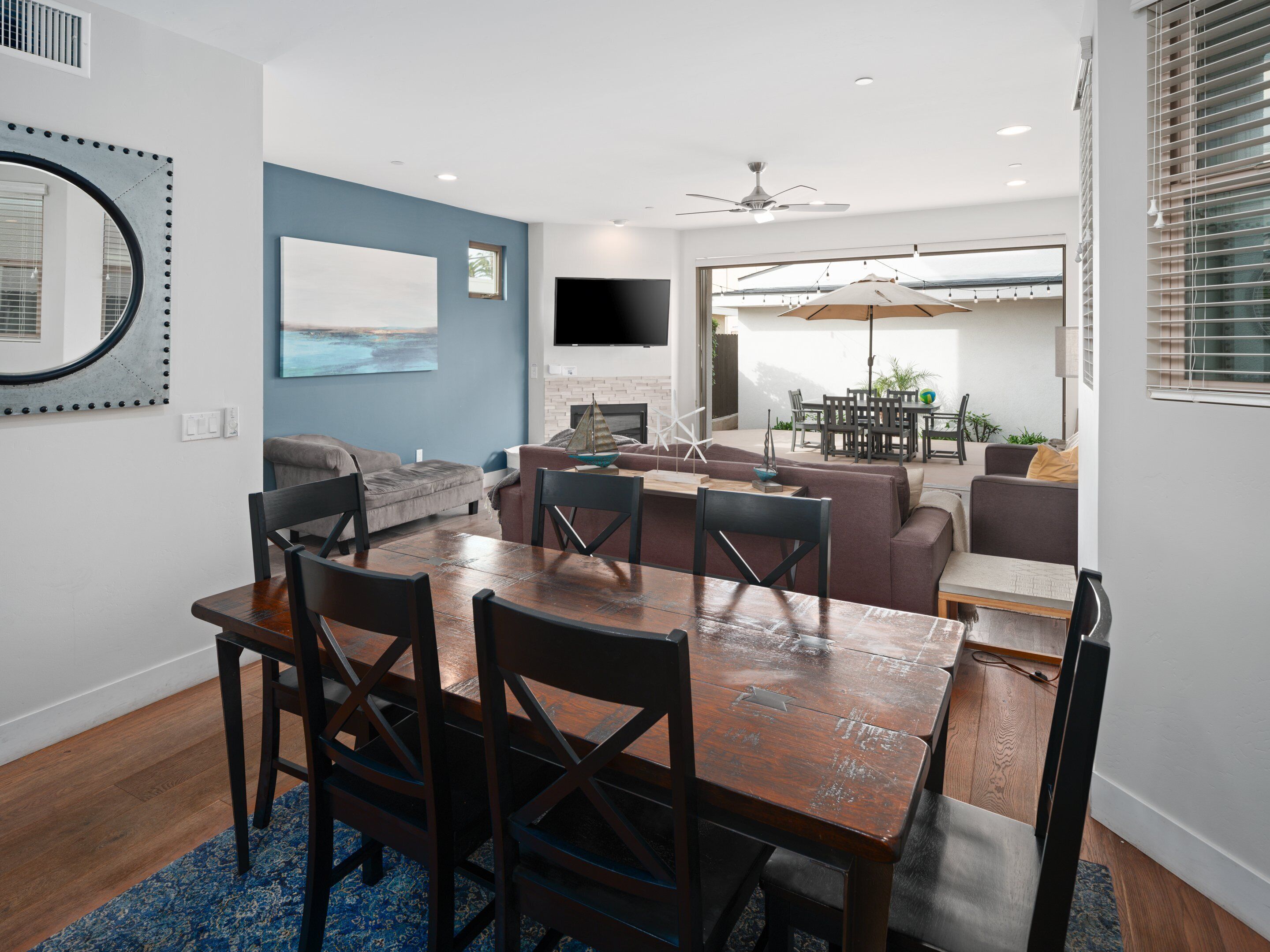 A modern living room with a dining area, a flat-screen TV mounted on the wall, and a ceiling fan.