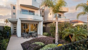 A modern multi-story house with a patio area, outdoor furniture, and a variety of plants. - Large Family Beach Home | 1 Block to Beach & More | AC (San Diego)