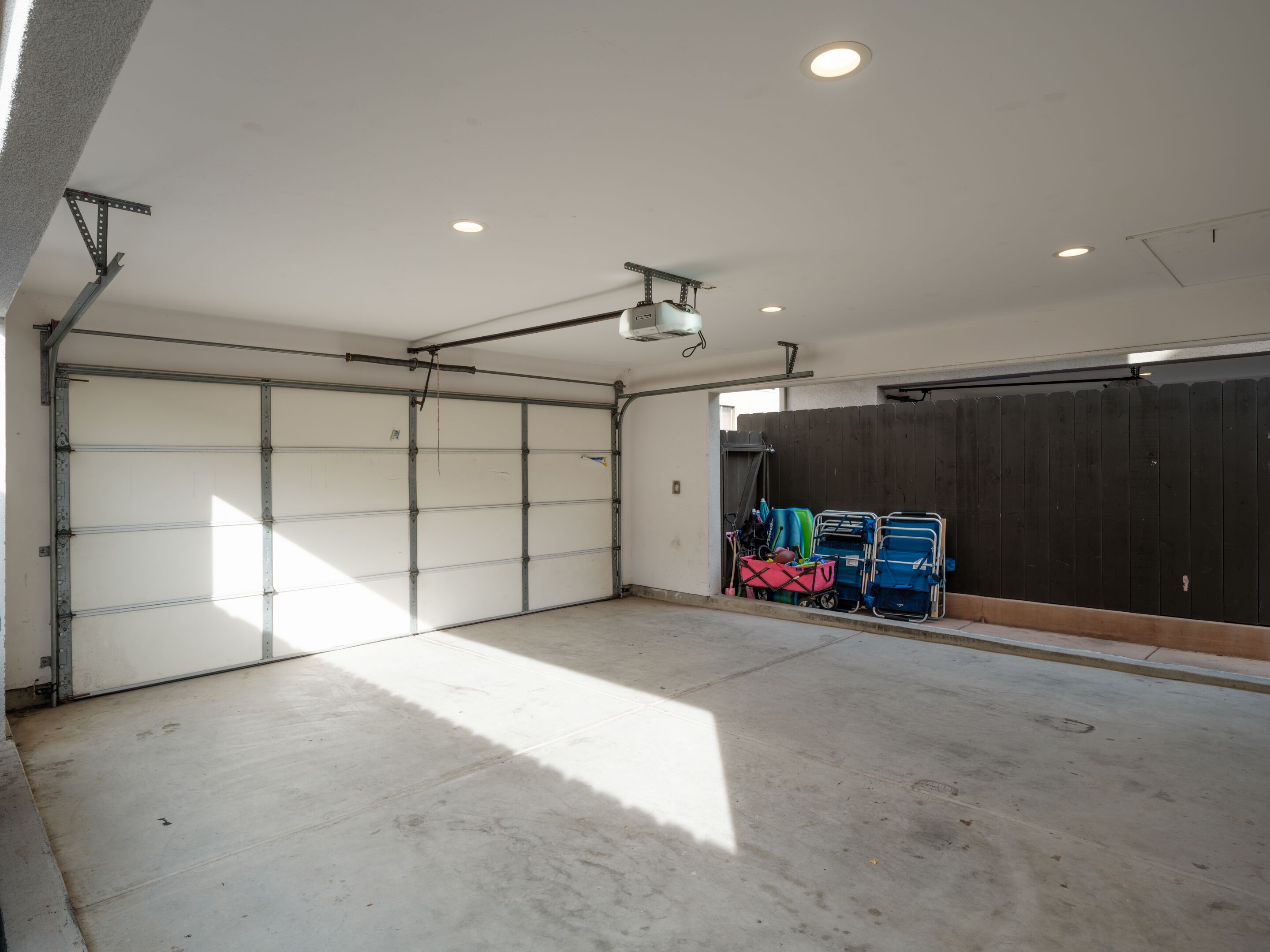 A garage with a concrete floor, a closed garage door, and a wooden fence.