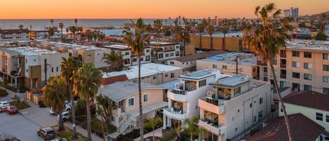 A residential area with modern apartment buildings, palm trees, and a view of the ocean at sunset.