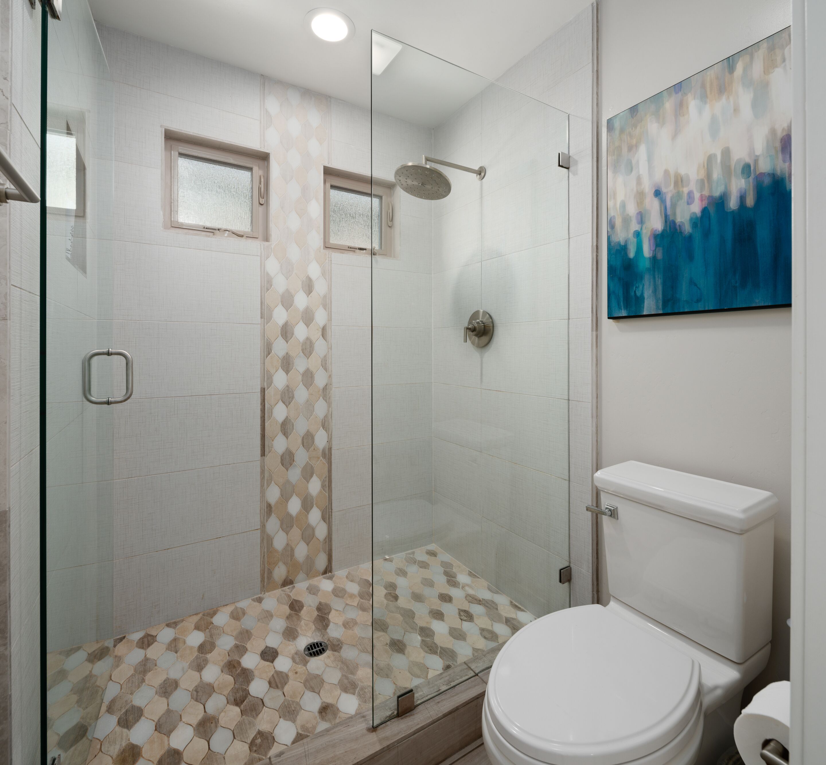A modern bathroom with a glass-enclosed shower, a toilet, and a large abstract painting on the wall.