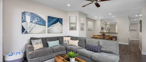 A modern living room with a gray sectional sofa, a wooden coffee table, and a ceiling fan.
