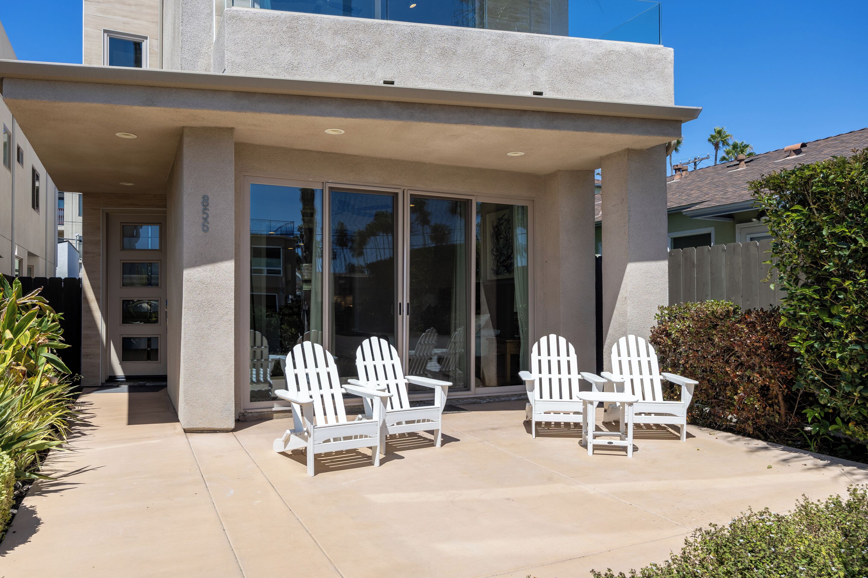 Un edificio moderno con un patio cubierto y sillas Adirondack blancas.
