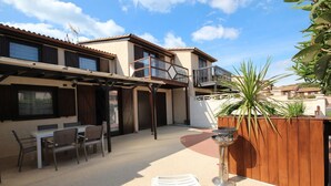 A patio area with a table and chairs, a wooden fence, and a plant. - Pleasant renovated fenced house with air conditioning, Wifi, DOMAINE TAMARIS, 3 bedrooms, sleeps... (PORTIRAGNES)