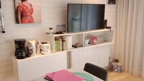 Ett modernt vardagsrum med en platt-TV, en kaffemaskin, böcker och dekorativa föremål på hyllor.