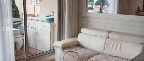 En stue med en hvid sofa, en sort lænestol, et lille bord med et lys og udsigt til den udendørs balkon.