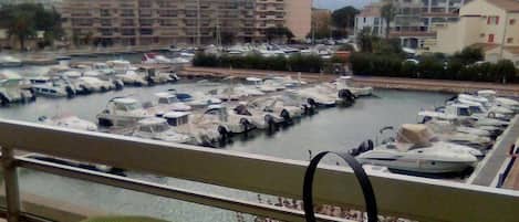 Un balcon donnant sur un port de plaisance, une table avec une théière et une tasse, et un chandelier.