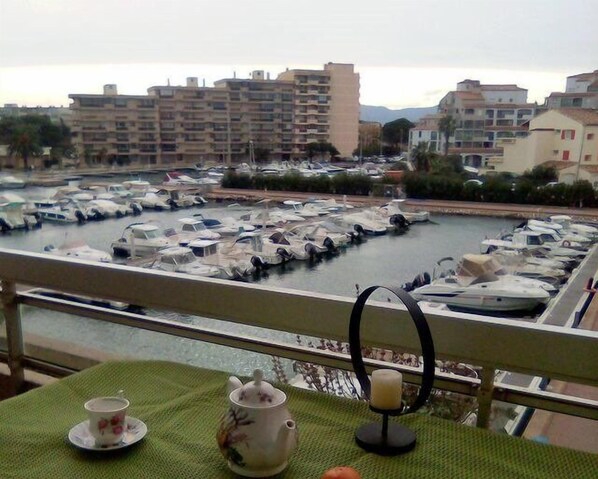 A balcony with a view of a marina, a table with a teapot and cup, and a candle holder.