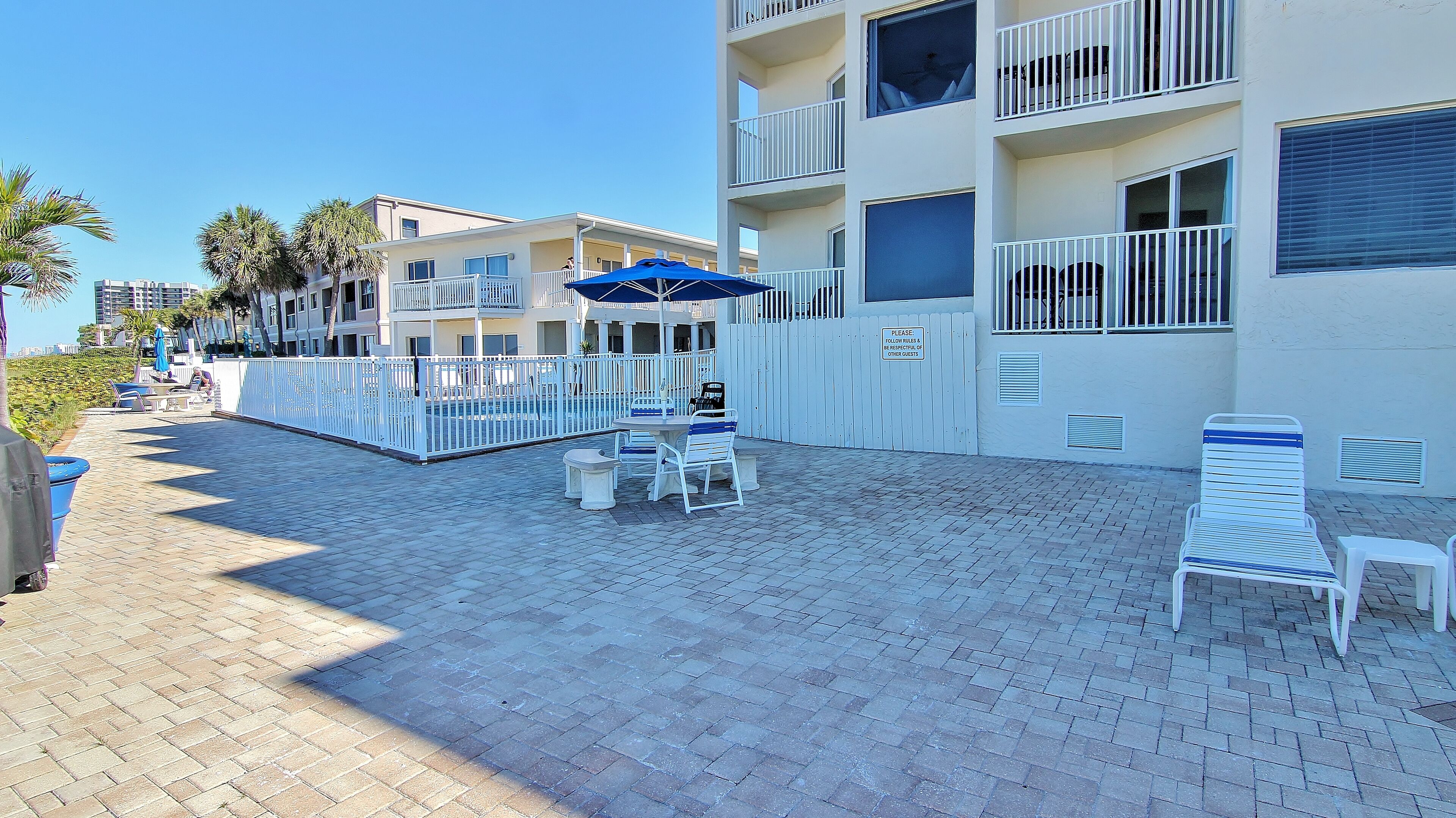 A hotel courtyard with outdoor seating, a pool, and a white fence.