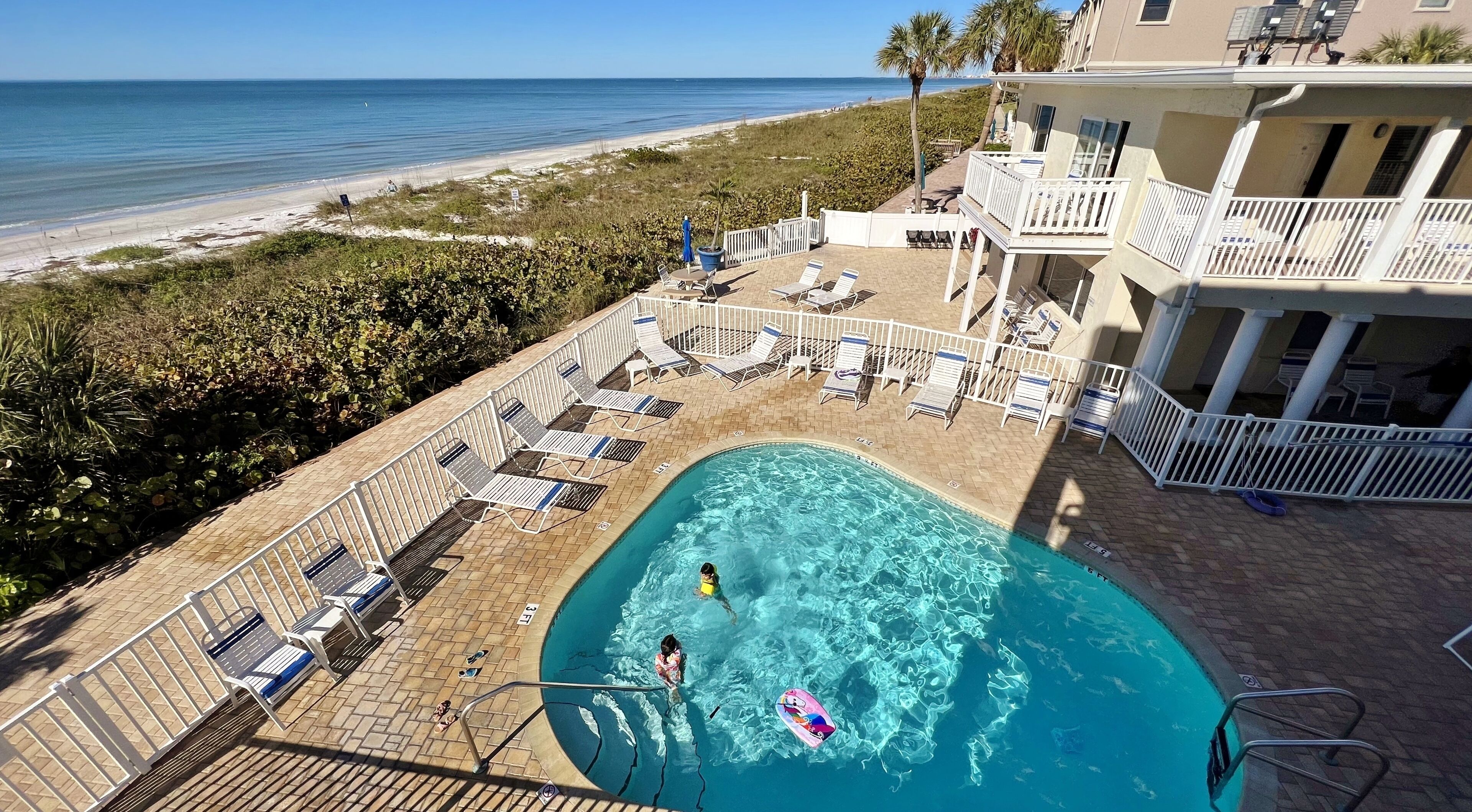 A pool area with lounge chairs and a view of the beach.