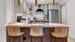 A modern kitchen with a central island, stainless steel appliances, and wicker bar stools.