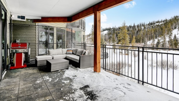 A covered outdoor area with a sofa and grill, overlooking a snowy landscape.