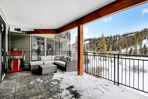 A covered outdoor area with a sofa and grill, overlooking a snowy landscape.