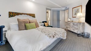 A hotel room with a large bed, a dresser, a chair, and a painting on the wall.