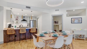 A modern kitchen with a central island, white chairs, and a dining table set for six.