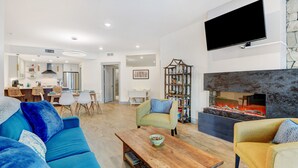 A modern living room with a sofa, armchairs, a coffee table, a fireplace, and a kitchen in the background.