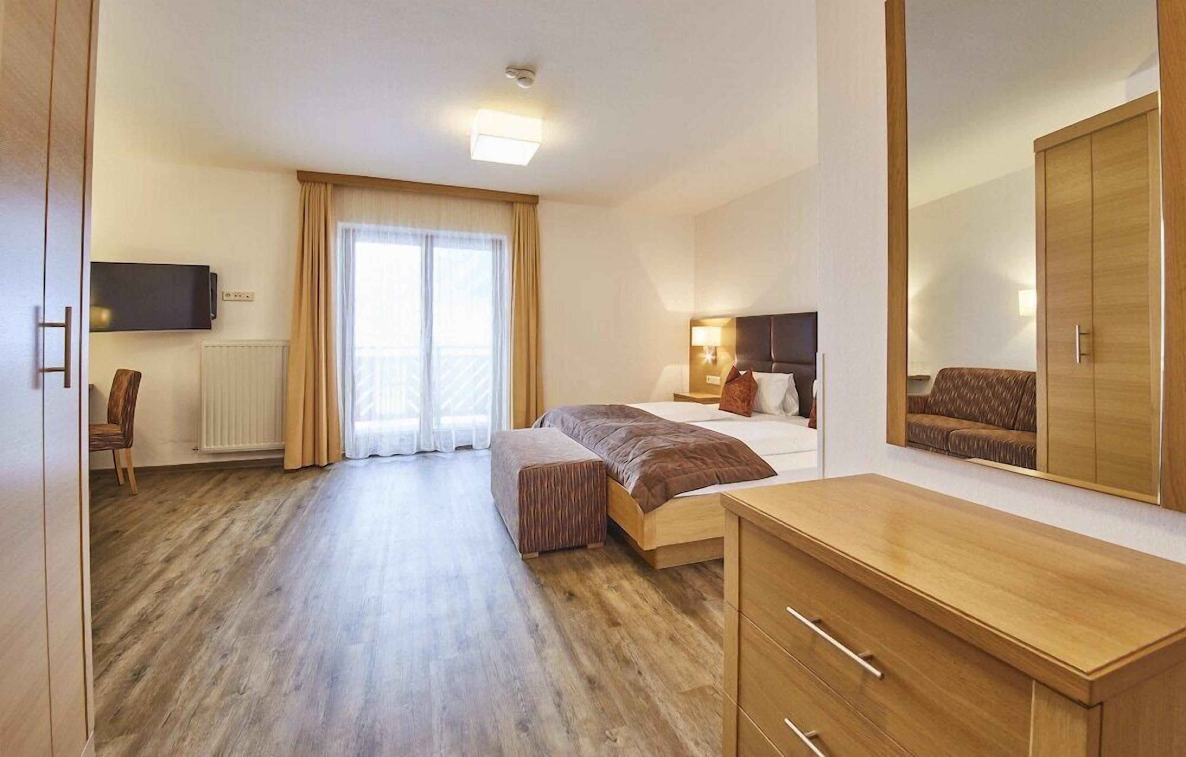 A hotel room with a bed, bedside table, lamp, wardrobe, and a television on the wall.
