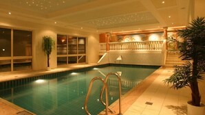 An indoor swimming pool with a tiled floor, a staircase leading to a balcony, and a railing.