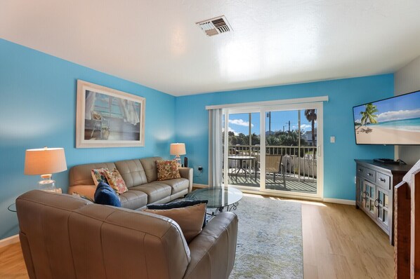 A living room with a blue wall, a brown leather sofa, a glass coffee table, and a TV on a cabinet.
