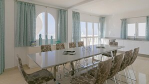 A spacious dining area with a long table and chairs, large windows with curtains, and a view of the sky. - Villa Panoramica (Costa Adeje)