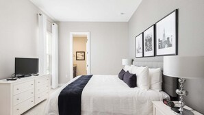 Une chambre d’hôtel moderne, équipée d’un lit, de tables de chevet, d’une télévision et de tableaux encadrés au mur.