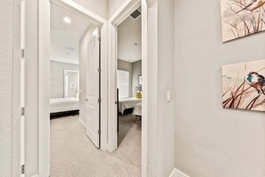 A hallway leading to a bedroom with a bed, a bedside table, and a window with blinds. - Ultra convenient stay > 5 min to Disney (Kissimmee)