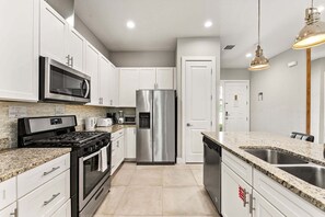A modern kitchen with white cabinets, stainless steel appliances, granite countertops, and pendant lighting. - Ultra convenient stay > 5 min to Disney (Kissimmee)