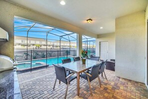 A covered patio with a pool, outdoor seating, and a grill.