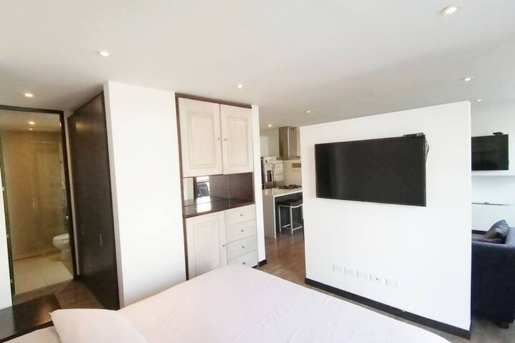 Habitació d'hotel moderna amb llit, televisió penjada a la paret, cuineta i bany.