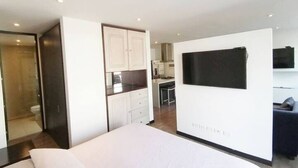 Moderni hotellihuone, jossa on sänky, seinälle asennettu televisio, pieni keittiö ja kylpyhuone.