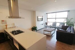 Una cocina moderna con una isla central, un comedor con sofá y sillas, y ventanas amplias que dejan entrar luz natural.