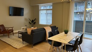 Ein modernes Wohnzimmer mit einer Couch, einem Esstisch mit Stühlen, einem an der Wand befestigten Fernseher und einem Deckenventilator.