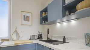 Une cuisine moderne avec un plan de travail en marbre, un évier noir et des armoires bleues. Un tableau encadré est accroché au mur, et il y a une fenêtre avec un rideau.
