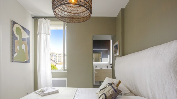 Une chambre avec un grand lit, une salle de bain avec un miroir et une vue sur les bâtiments à travers la fenêtre.
